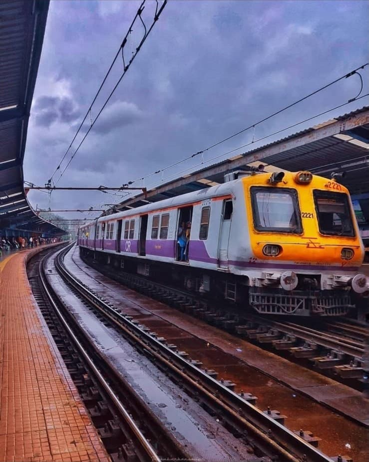 A local train pulling into the platform under monsoon skies
