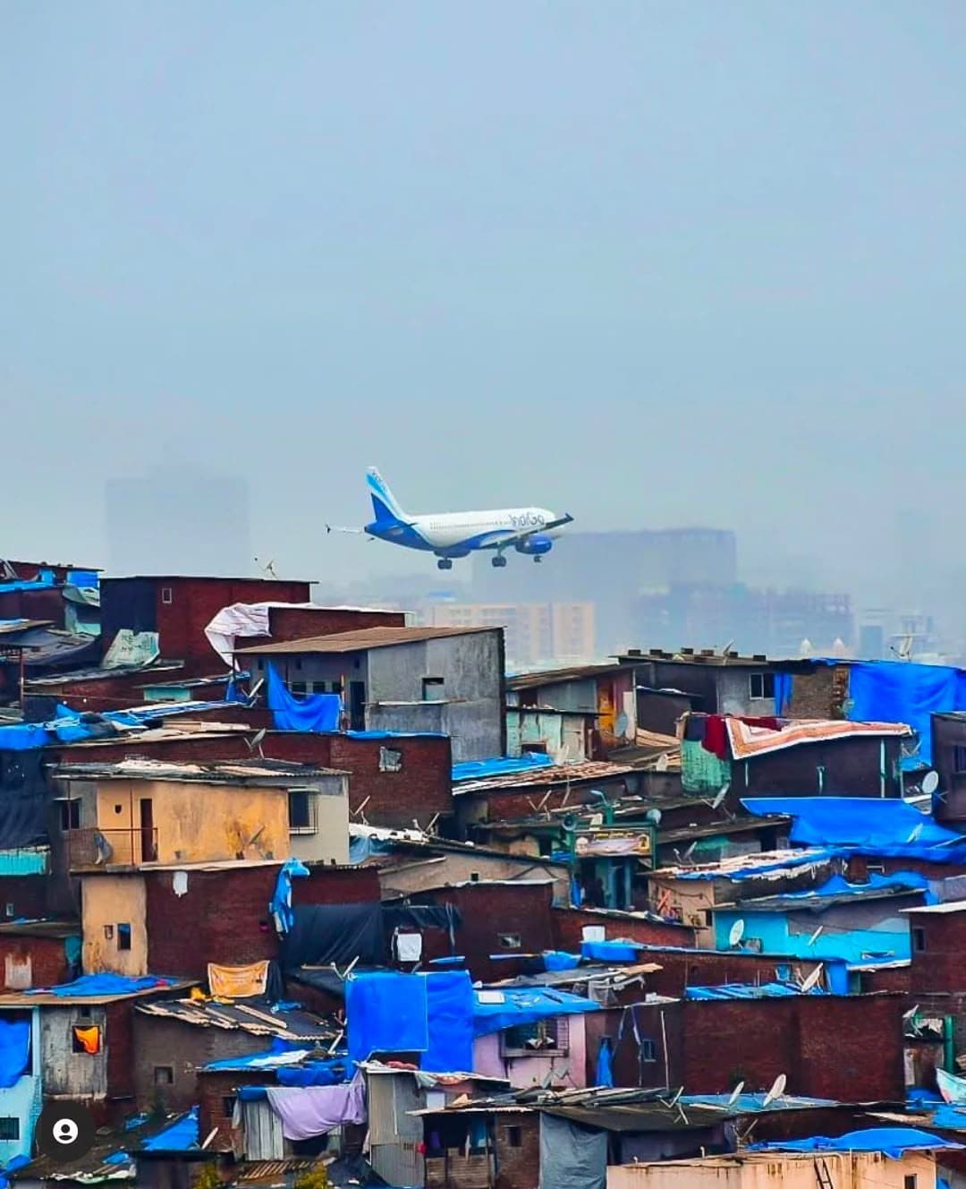 Blue tarpaulin rooftops of Dharavi with a plane landing overhead